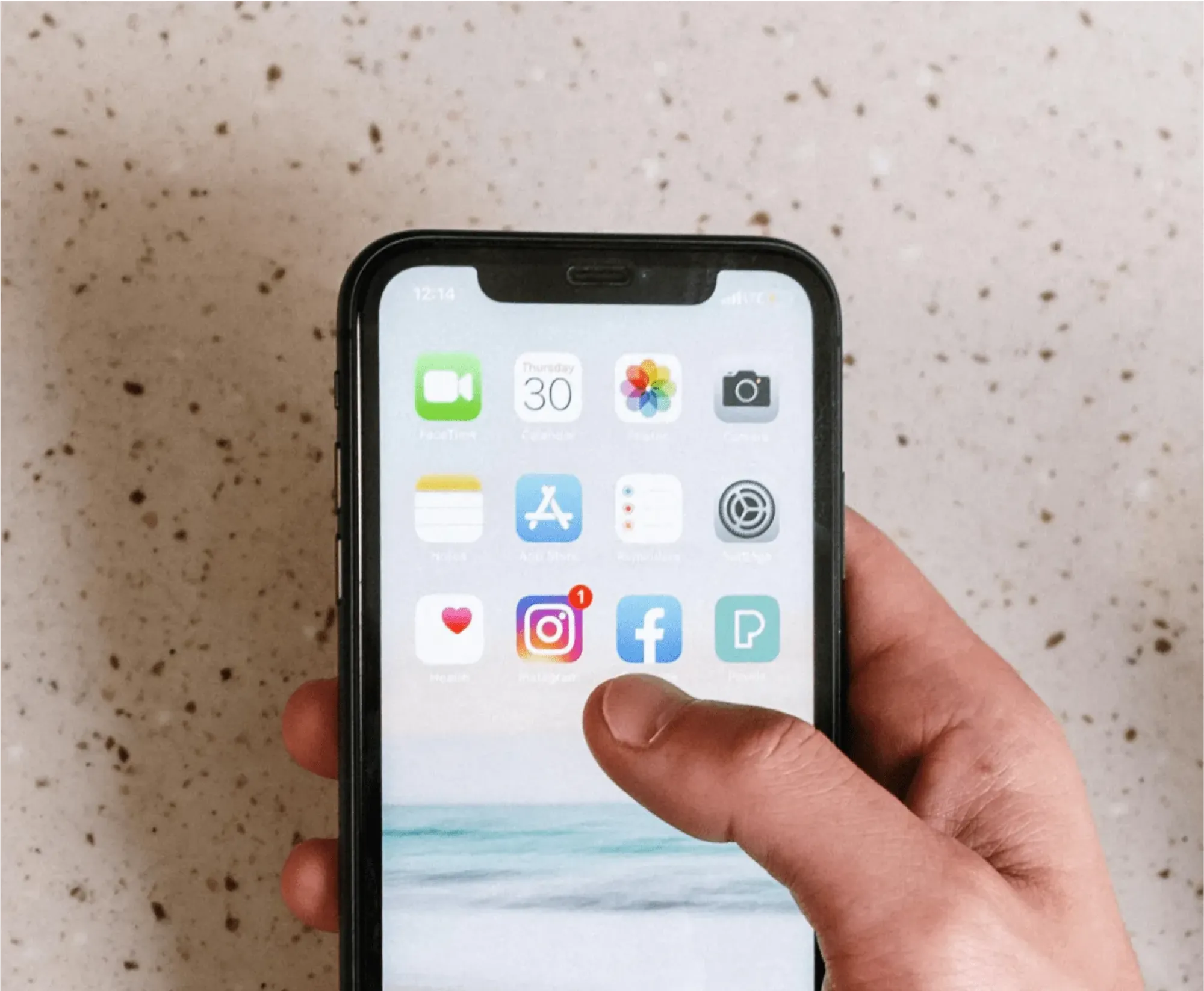 A person holding an iPhone displaying social media icons, related to managing a deceased person's Facebook account.