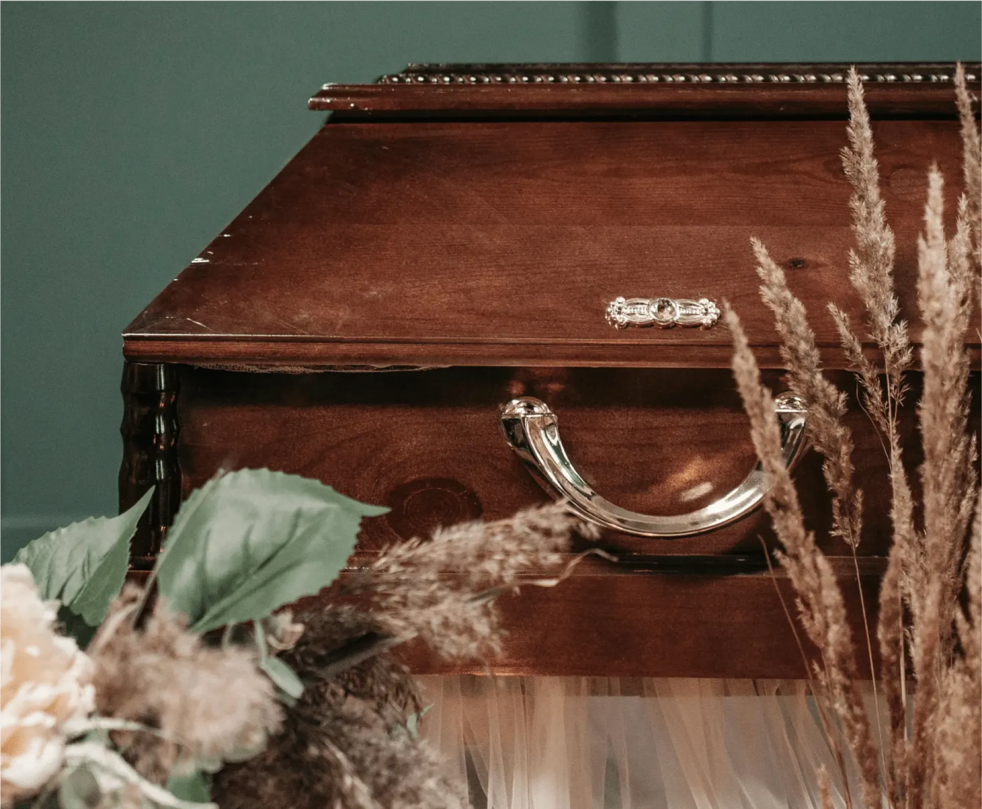 A wooden trunk with a handle adorned with flowers, placed at a graveside service for a meaningful memorial.