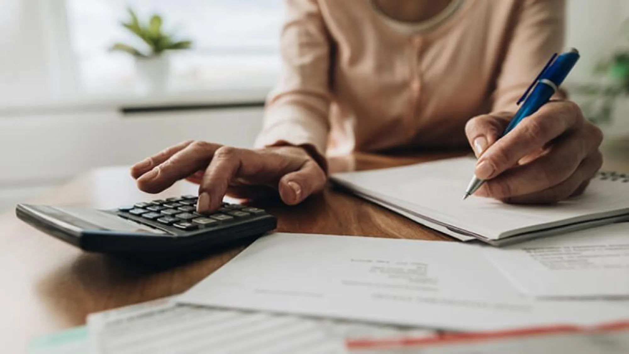 Woman writing on paper with a calculator and pen, contemplating credit card debt and its implications after death.
