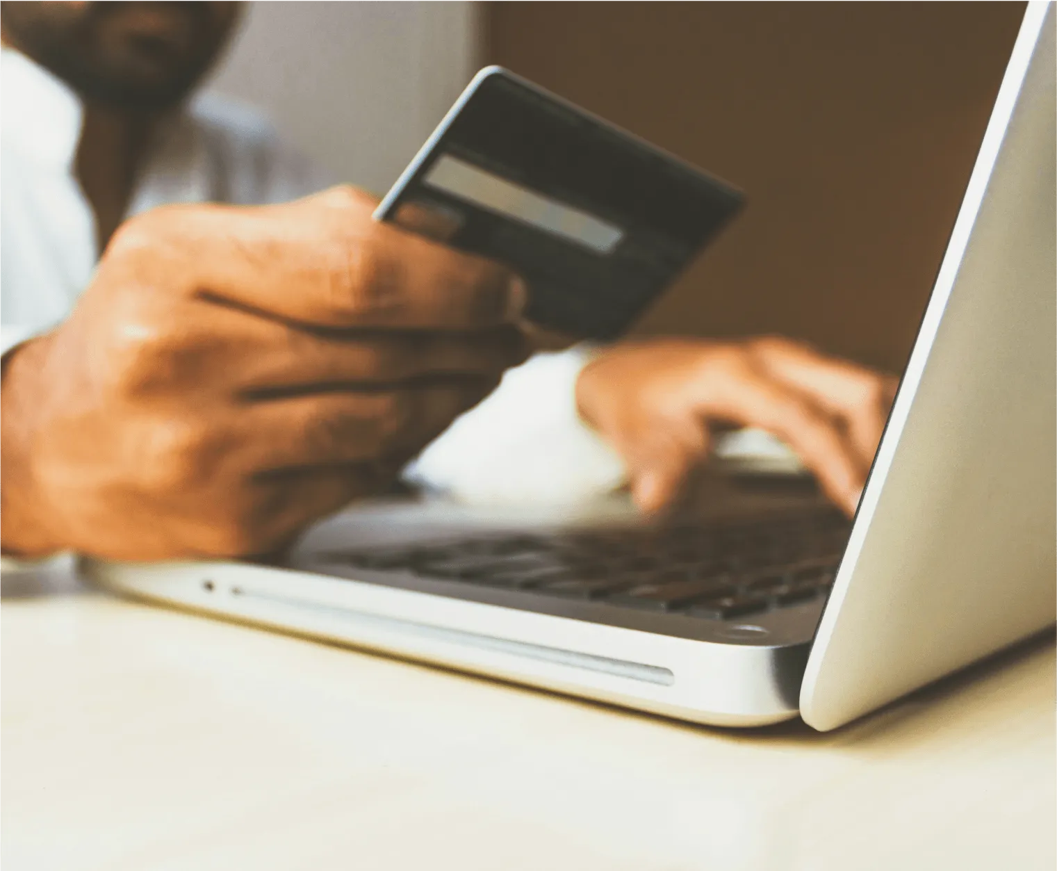A man using a laptop while holding a credit card, symbolizing online banking and account management after a loss.