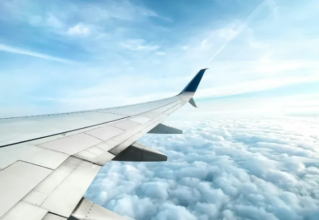 An airplane wing soaring above fluffy white clouds, symbolizing travel and connection in the sky.