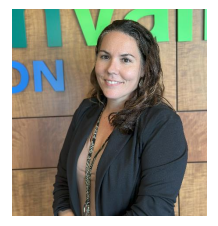Woman with light brown hair wearing a white blouse sitting on a sofa with folded hands, smiling gently.