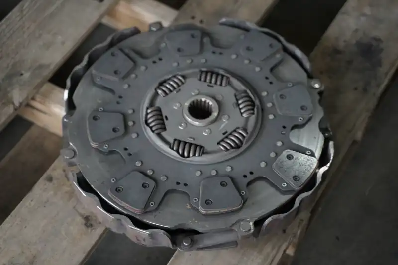 Flywheel and multi-puck clutch disc on floor jack under lifted truck, QR sticker visible, awaiting drivetrain reassembly.