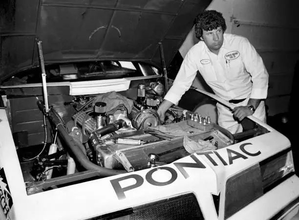 Waddell Wilson inspecting the engine compartment of a Pontiac race car