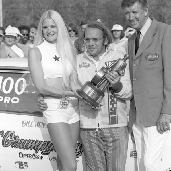 Bill Jenkins holding an NHRA trophy beside his Grumpy's Toy race car