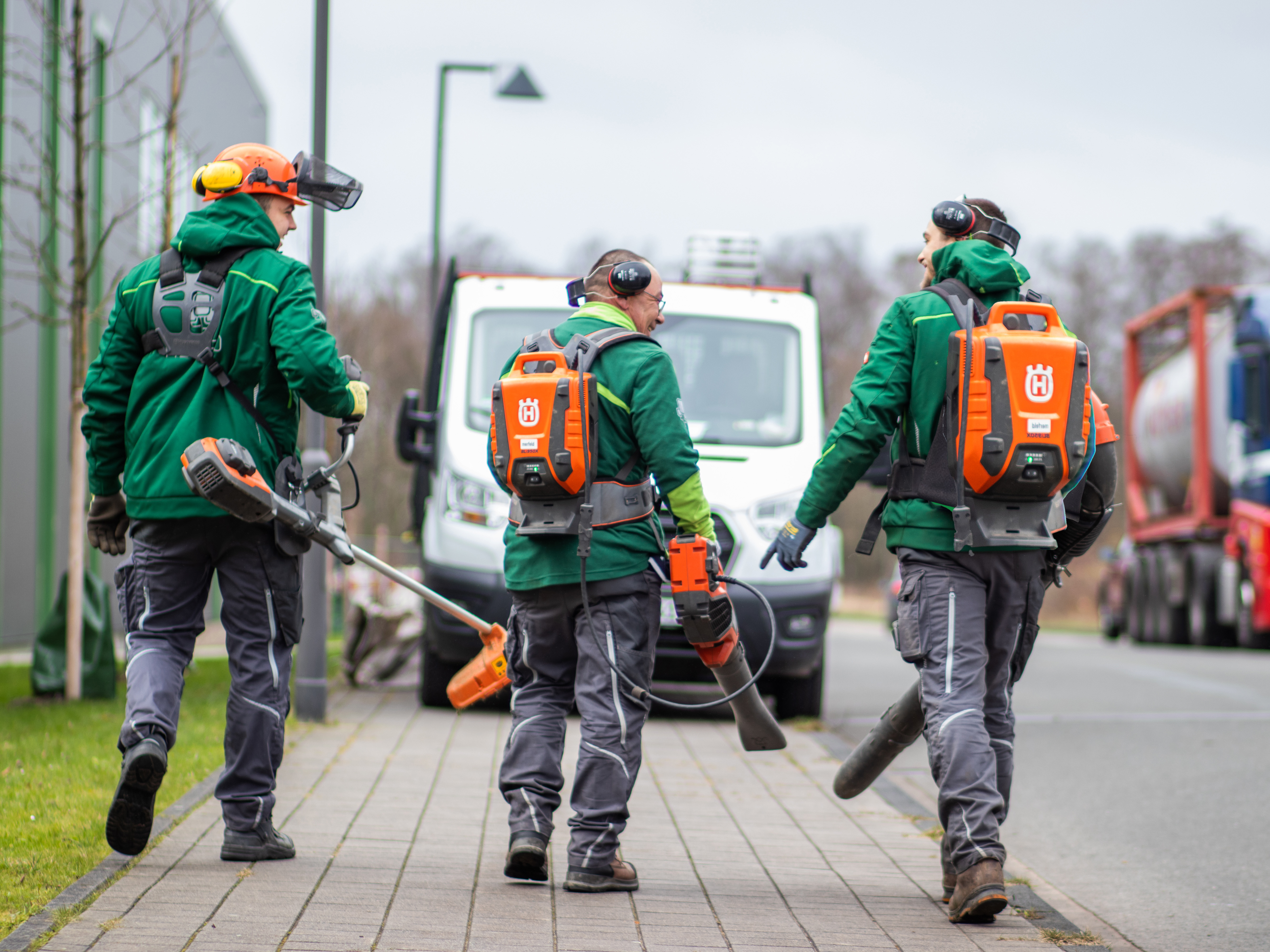 3 Mitarbeiter mit Akkus für die Laubbläser auf dem Rücken.
