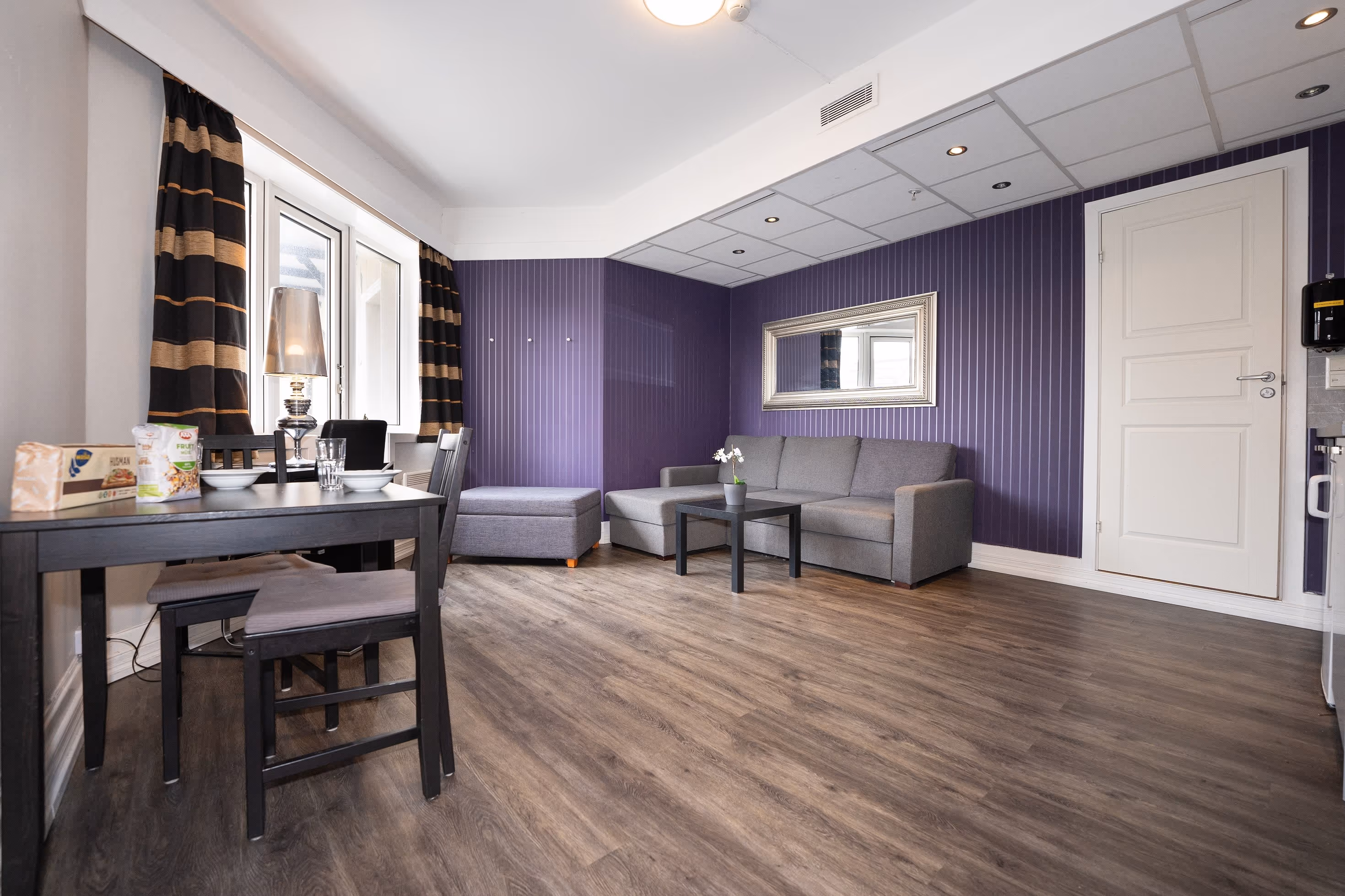 Stue med lilla vegg, sofa og spisegruppe.