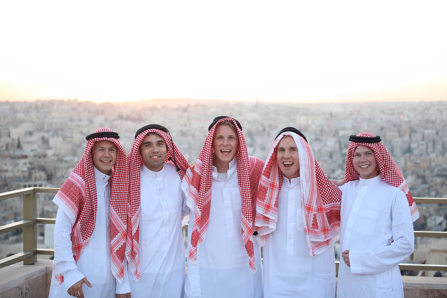 Fem bibelskoleelever i arabiske kjortler og røde hodeplagg foran solnedgangen i Jordan.