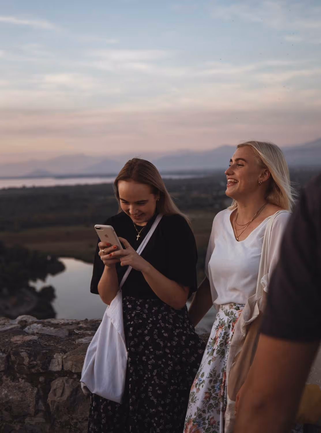 To jenter som smiler foran et landskap i solnedgang.