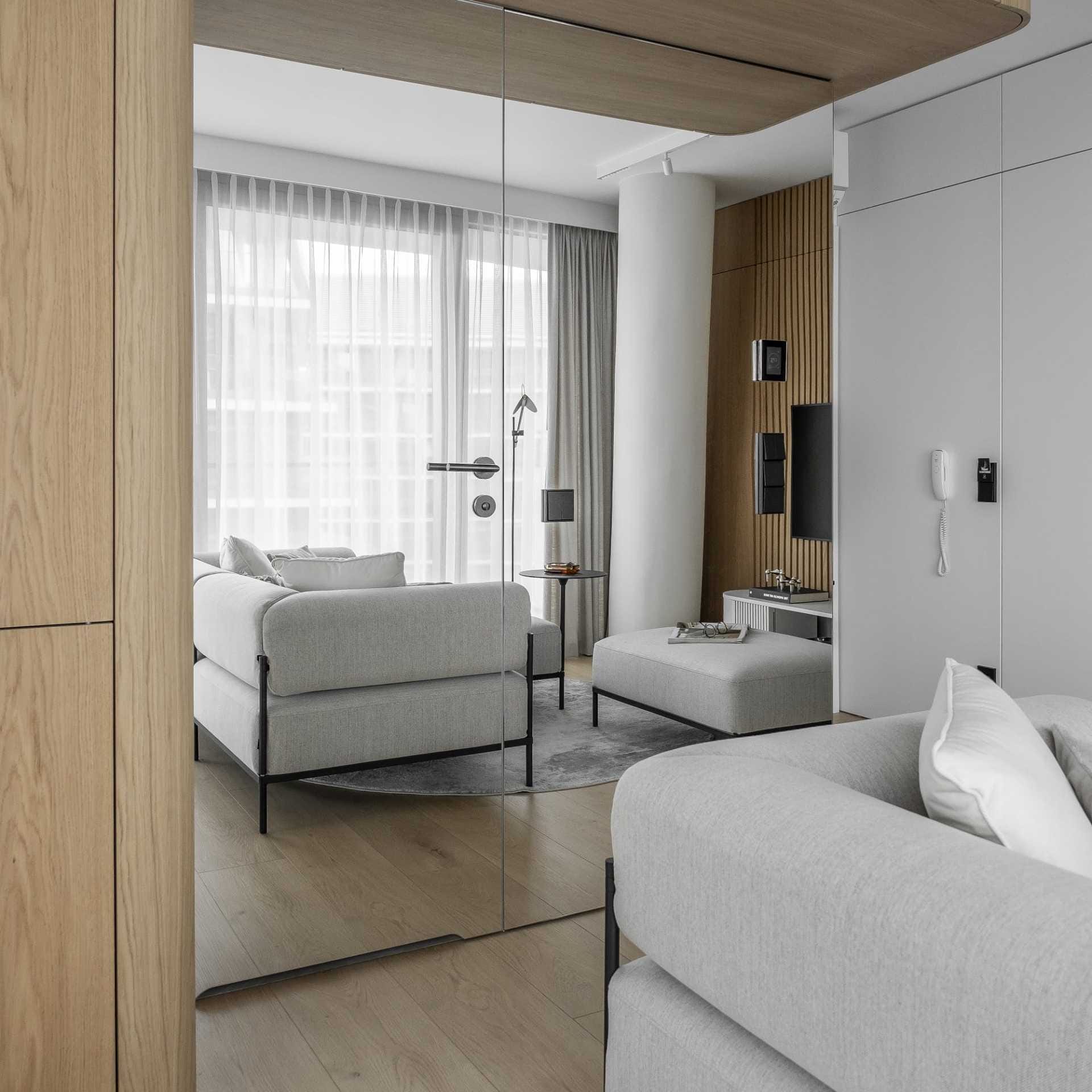 Nowoczesny salon z firanami i szarymi zasłonami odbity w lustrze, szarą sofą i drewnianymi lamelami – realizacja dekoracji okiennych na wymiar Hanna Szlachetko we współpracy z Mindful Architekci
