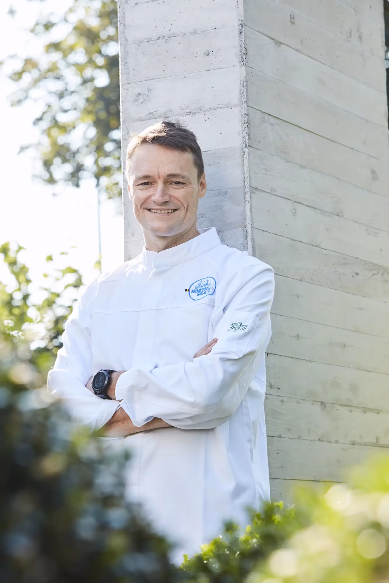 Filip Claeys porte un gilet de chef blanc avec le logo de Northseachef adossé à un mur gris.