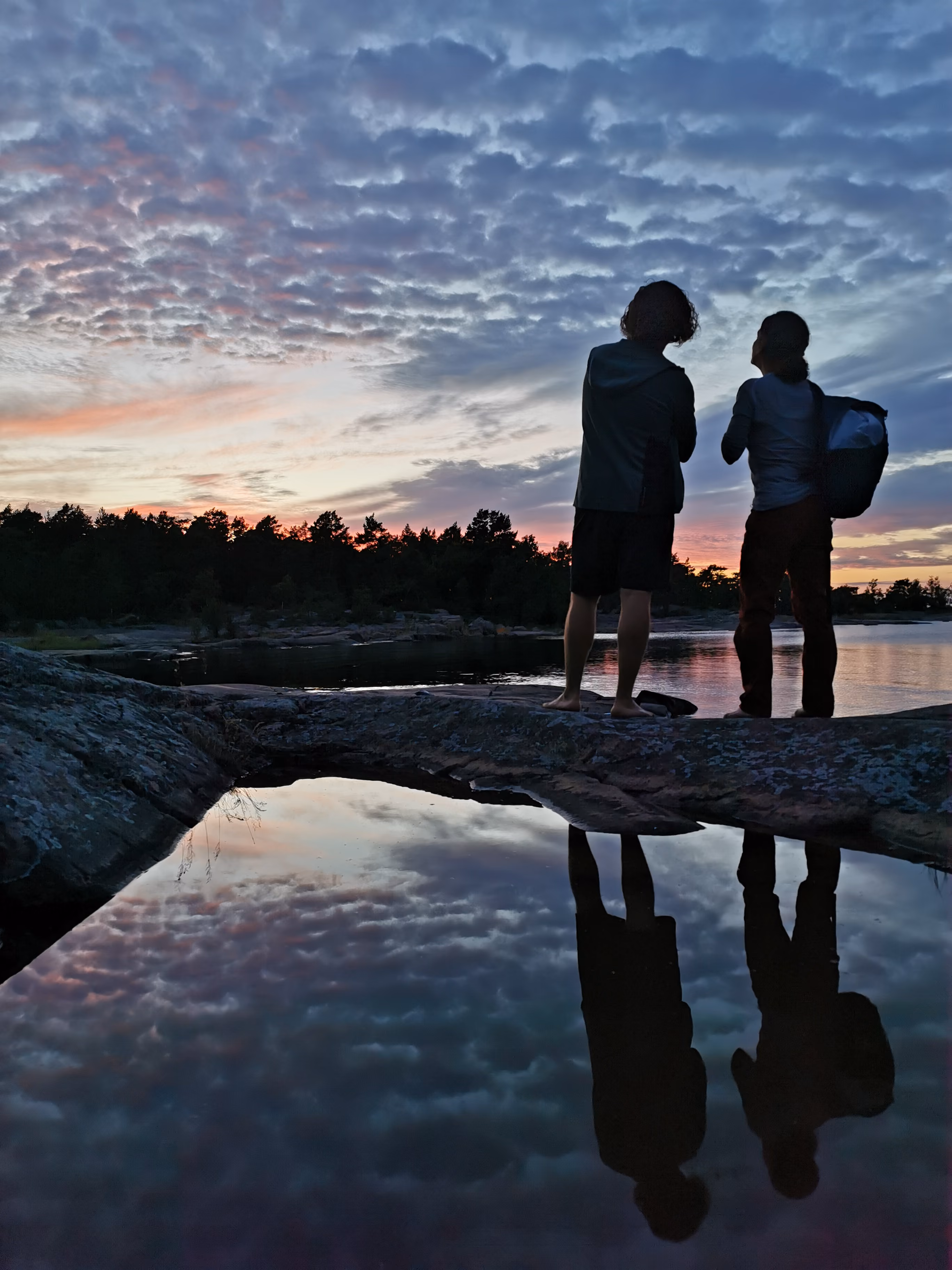 Two people at dawn watching the sunset over the ocean and talking being reflected in the water-