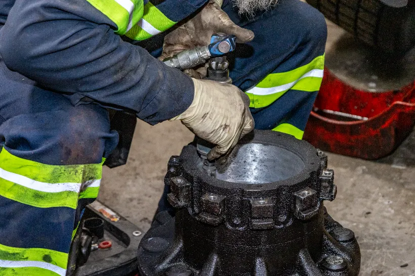 Worn brakes on heavy-duty wheel hub being serviced with air tool by gloved technician in repair bay.