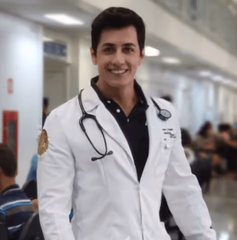 Smiling male doctor in white coat with stethoscope around neck in a hospital corridor.