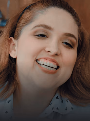 Smiling woman with light skin, reddish brown hair, and a black headband, wearing a white shirt.
