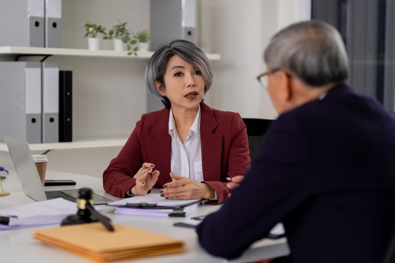 Asian adult woman lawyer consults client modern office. Expert provides professional legal advice. Important business meeting with paperwork.