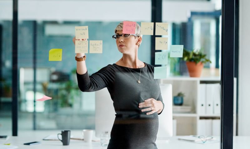Pregnant woman organizing notes on a glass wall in a modern office