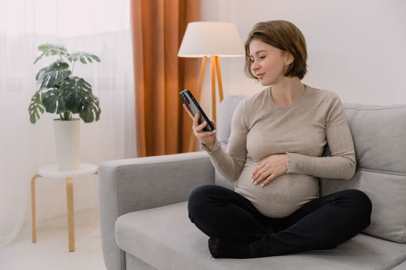 Pregnant woman sitting on a couch at home looking at her phone. Contact Frontier Center for a free pregnancy discriminatio Lawn consultation