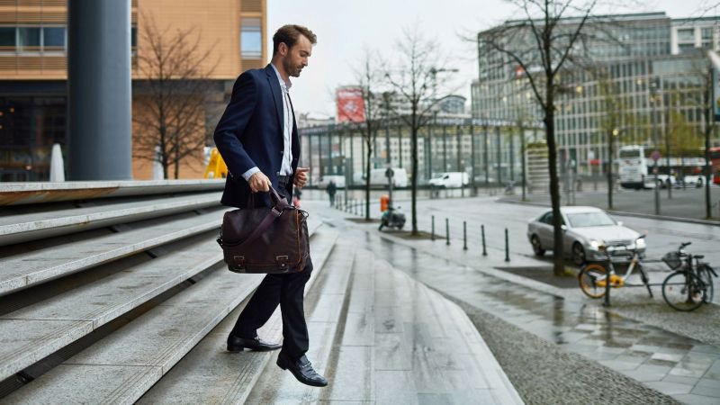 Professional man carrying a bag walking down steps outside a commercial building, leaving the workplace after a layoff or termination in California