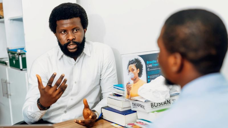 A man in a white shirt speaks expressively across a desk during a serious one-on-one conversation