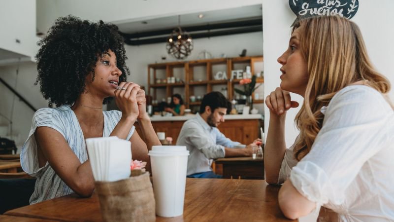 Two women have a candid conversation at a California café, one listening attentively while the other speaks