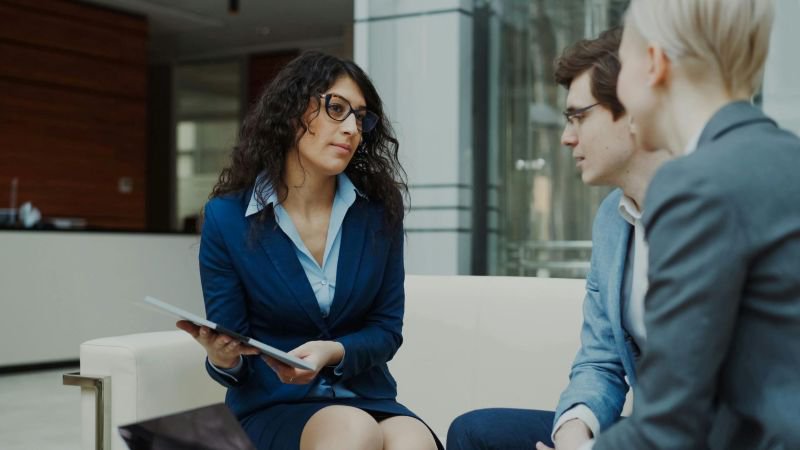 A woman of Middle Eastern descent leads a professional consultation with two colleagues in a modern California office setting