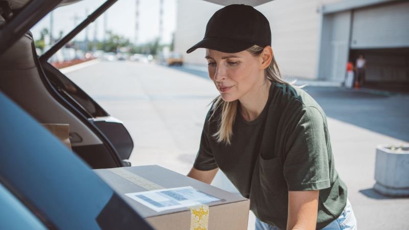 Female delivery driver loading a package into her car trunk, representing gig economy misclassification in California
