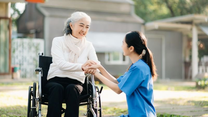 Daughter holding hands with elderly mother in wheelchair outdoors, representing CFRA caregiving leave in California