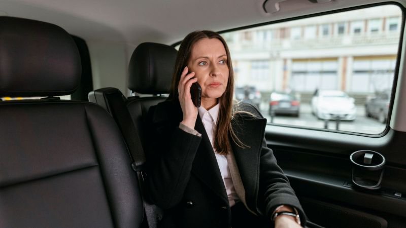 A woman in professional attire making a phone call while seated in a car, representing an employee reaching out privately about a sexual harassment case in California