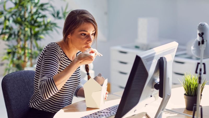 Employee eating takeout at her desk while working, illustrating a common California break laws violation