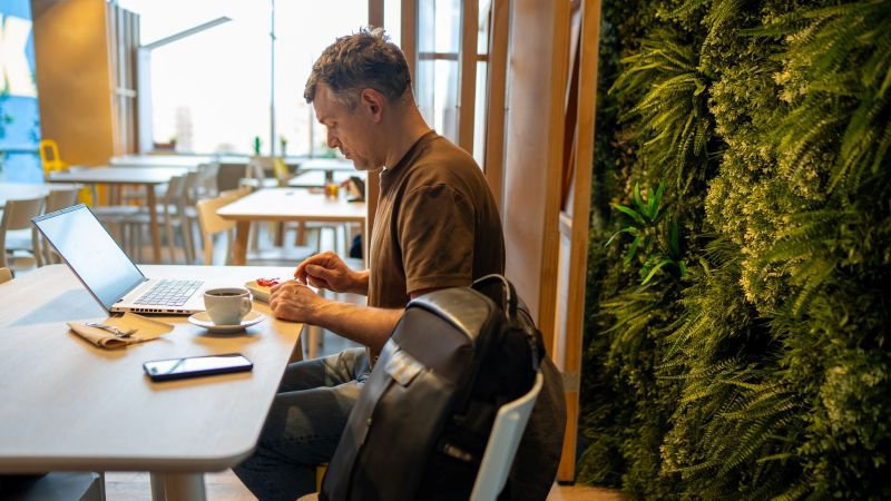 Employee eating at a table with a laptop and phone nearby, unable to step away from work during a meal period