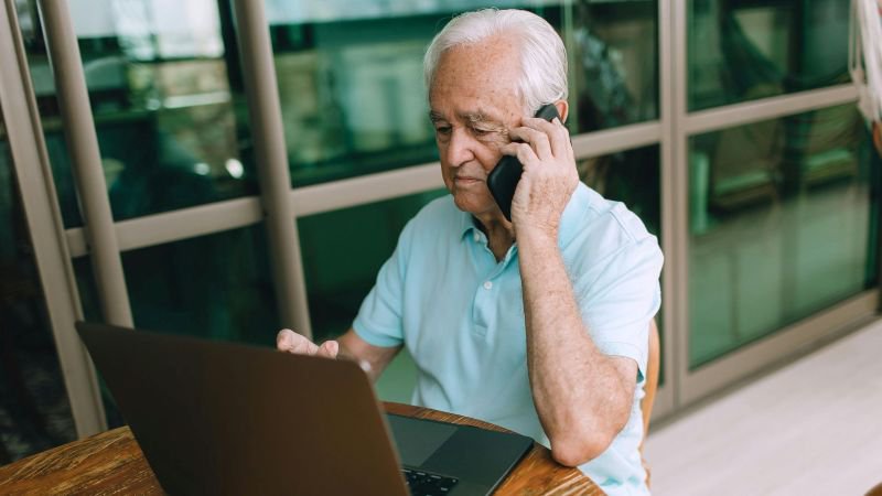 Senior professional on a phone call while reviewing a laptop outside