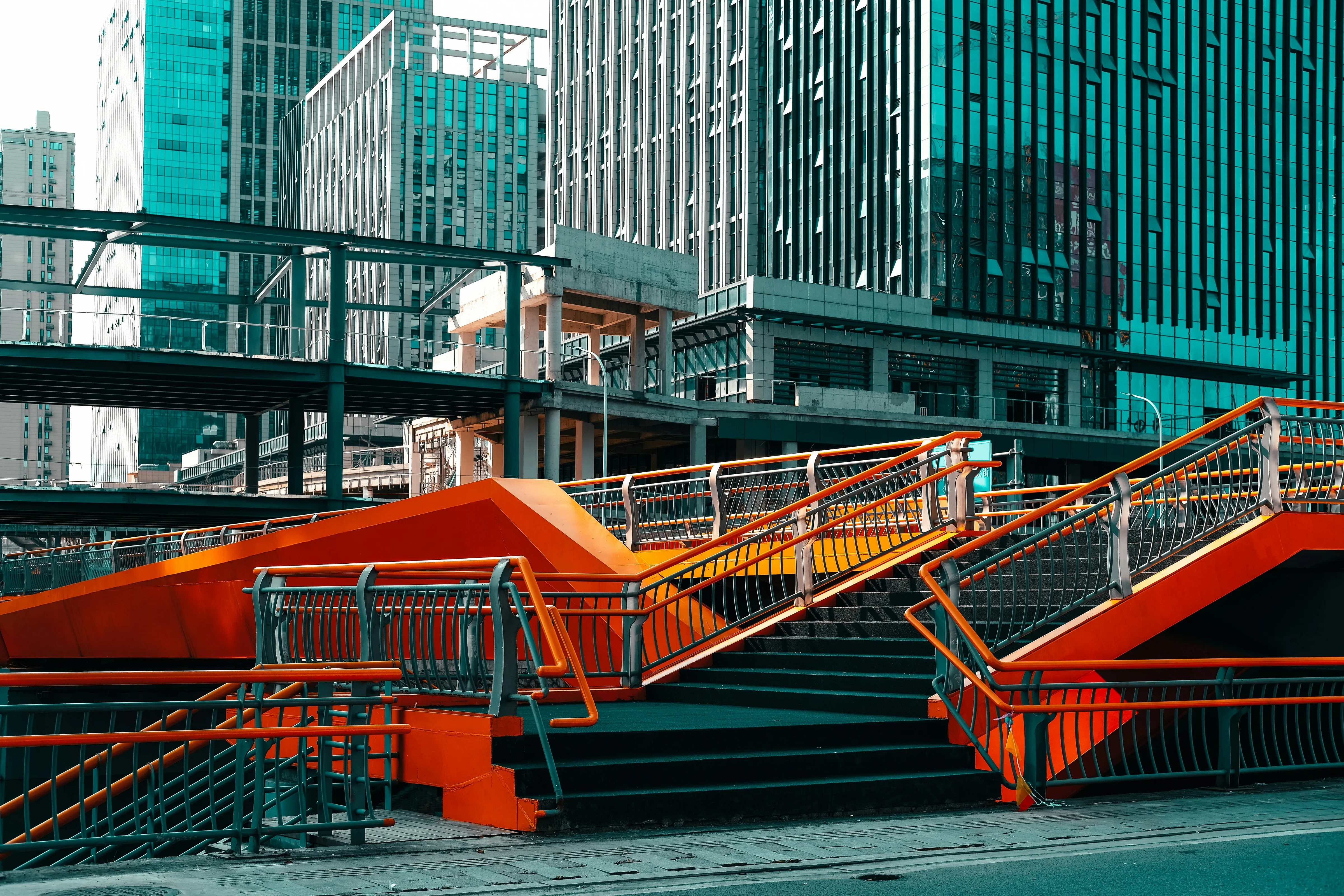 A vibrant staircase with orange railings set against a backdrop of urban skyscrapers.