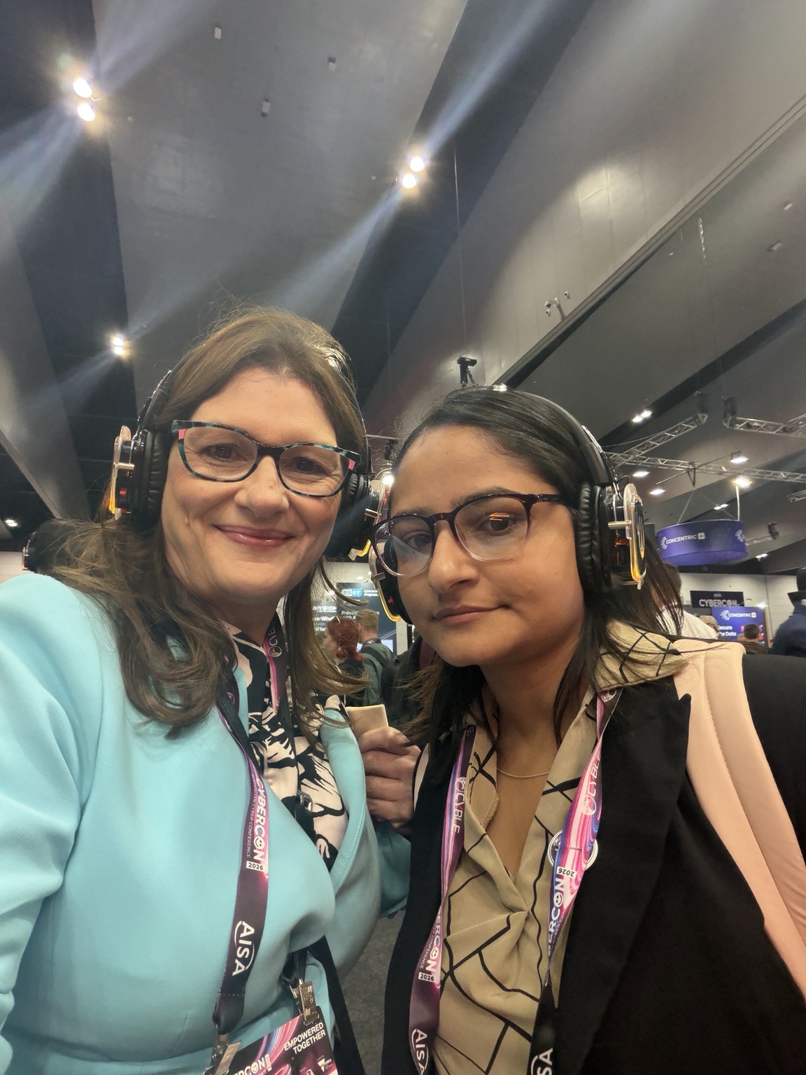 Louise and Anisha wearing headphones on the CyberCon 2026 exhibition floor
