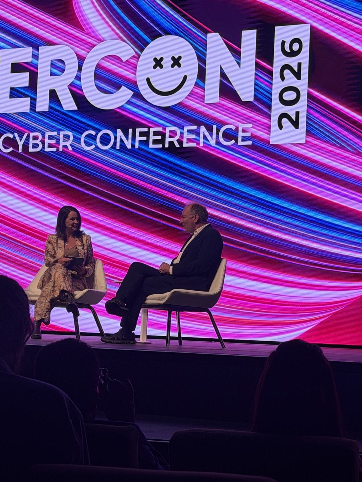 A conversation on stage beneath the CyberCon 2026 conference screen