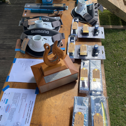 Wooden prize trophy with hook design on a table alongside Shimano fishing packages.
