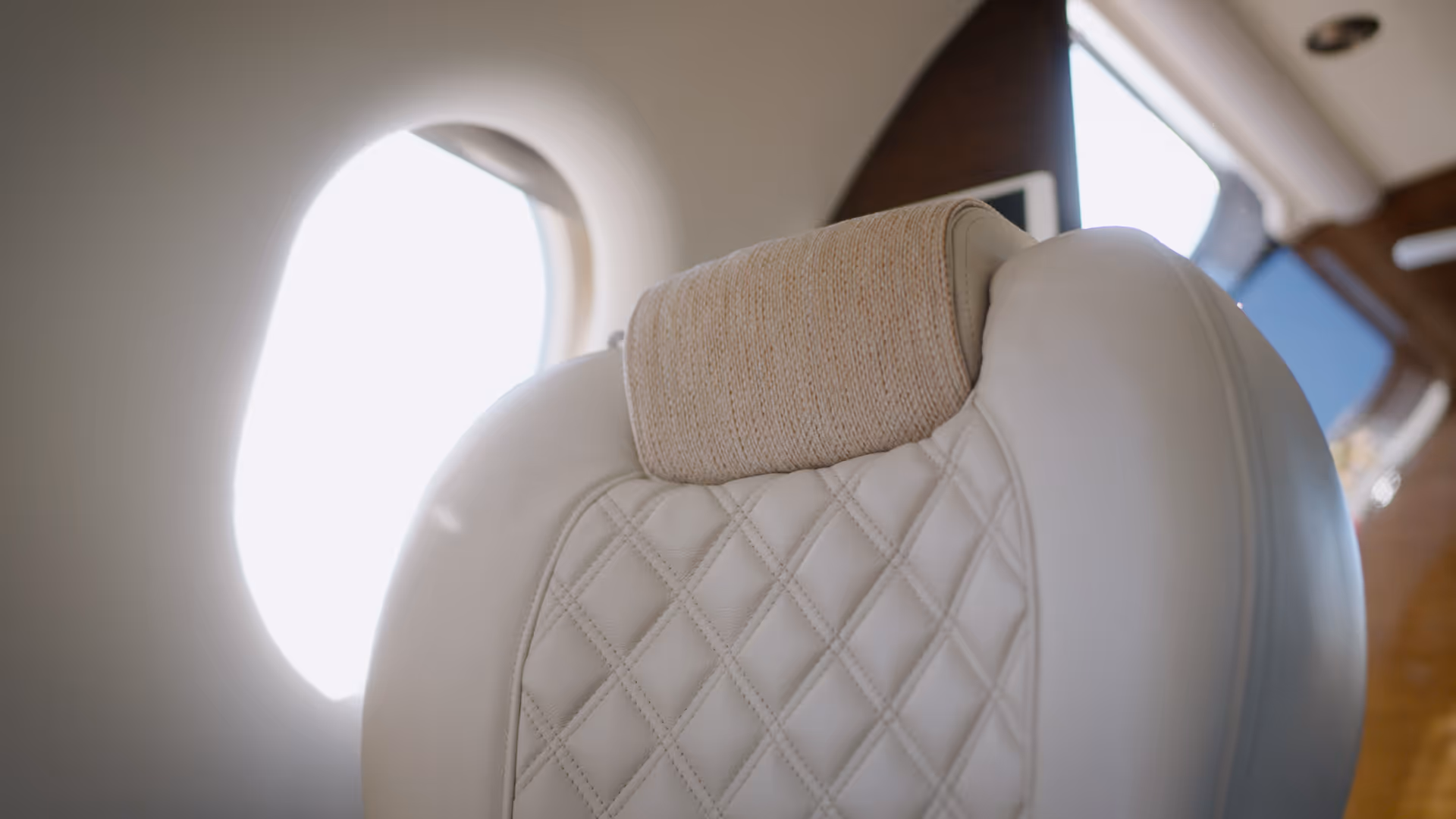 Close-up of luxurious white leather aircraft seat with quilted stitching inside private jet cabin.