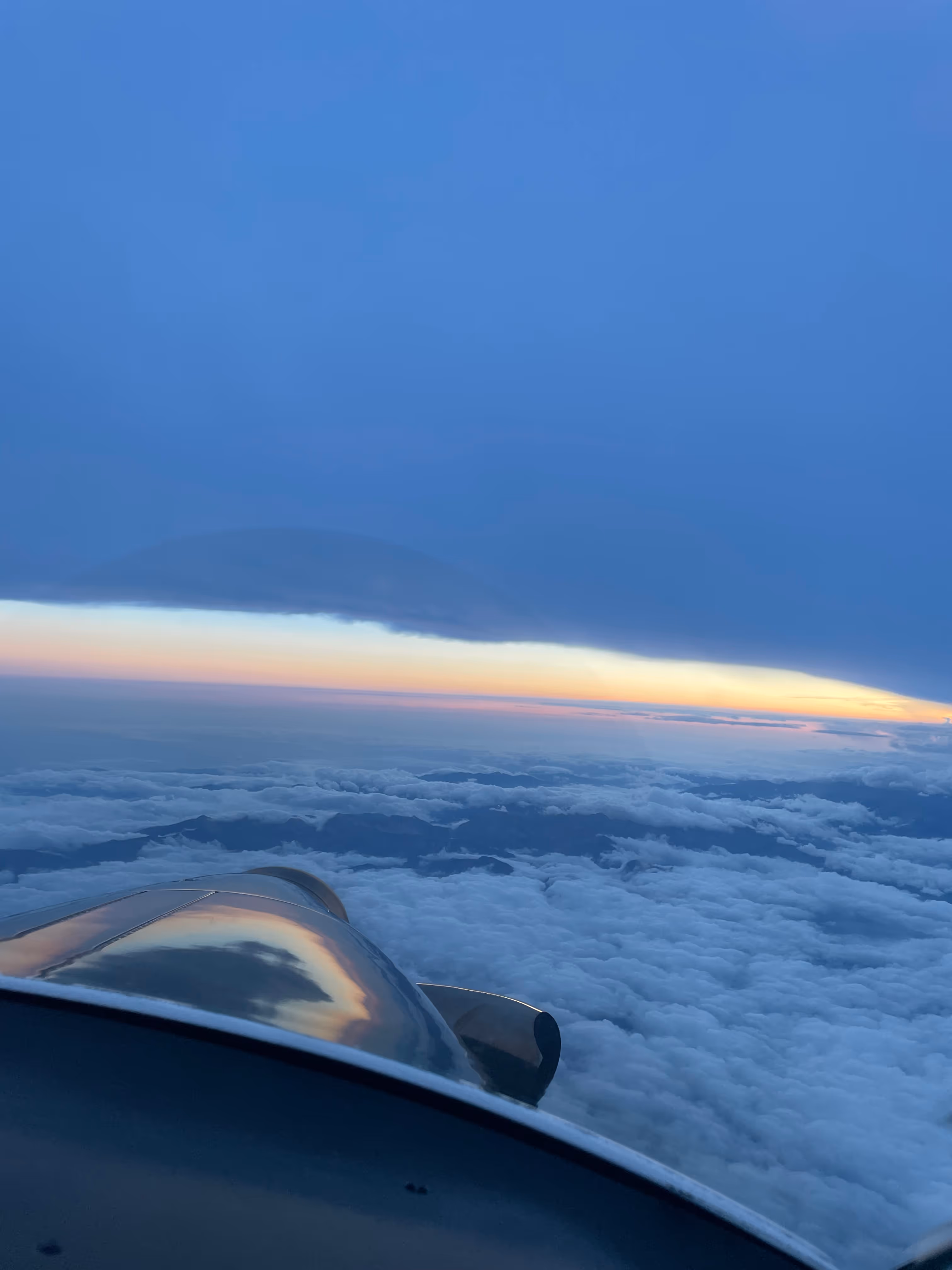 Sunset view from cockpit above the clouds with aircraft nose reflecting light.