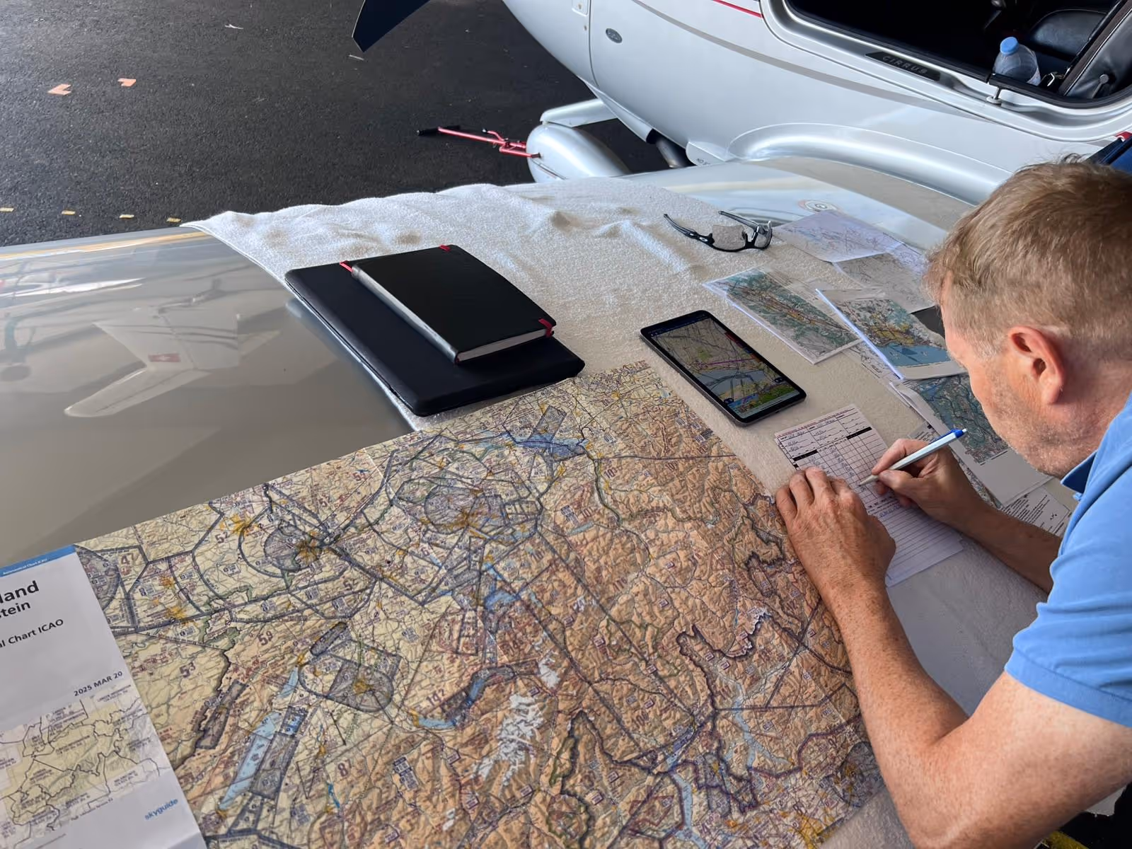 Pilot planning flight with aviation charts, maps, and tablet on aircraft wing.