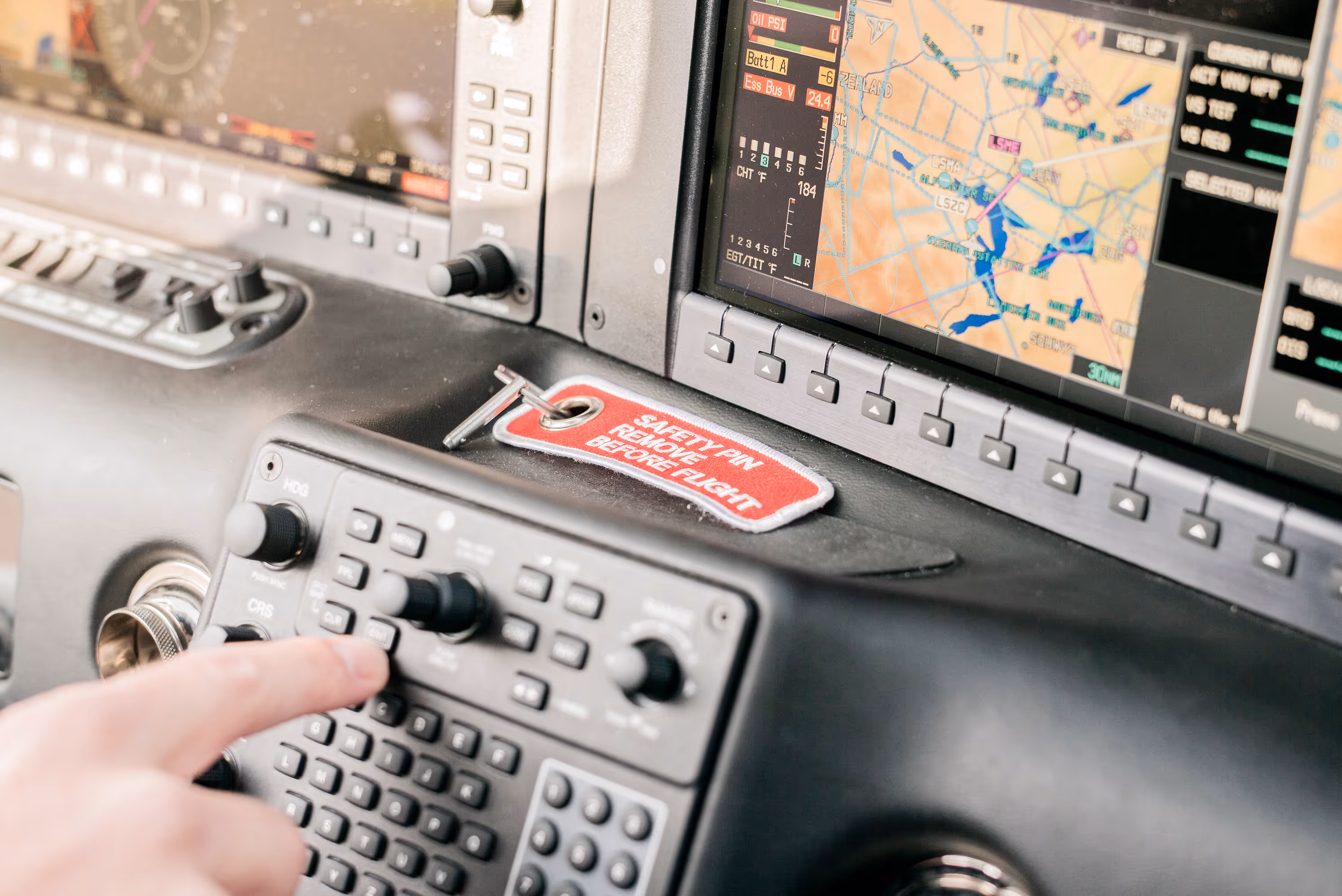 Finger pressing avionics control panel button with navigation displays in cockpit.