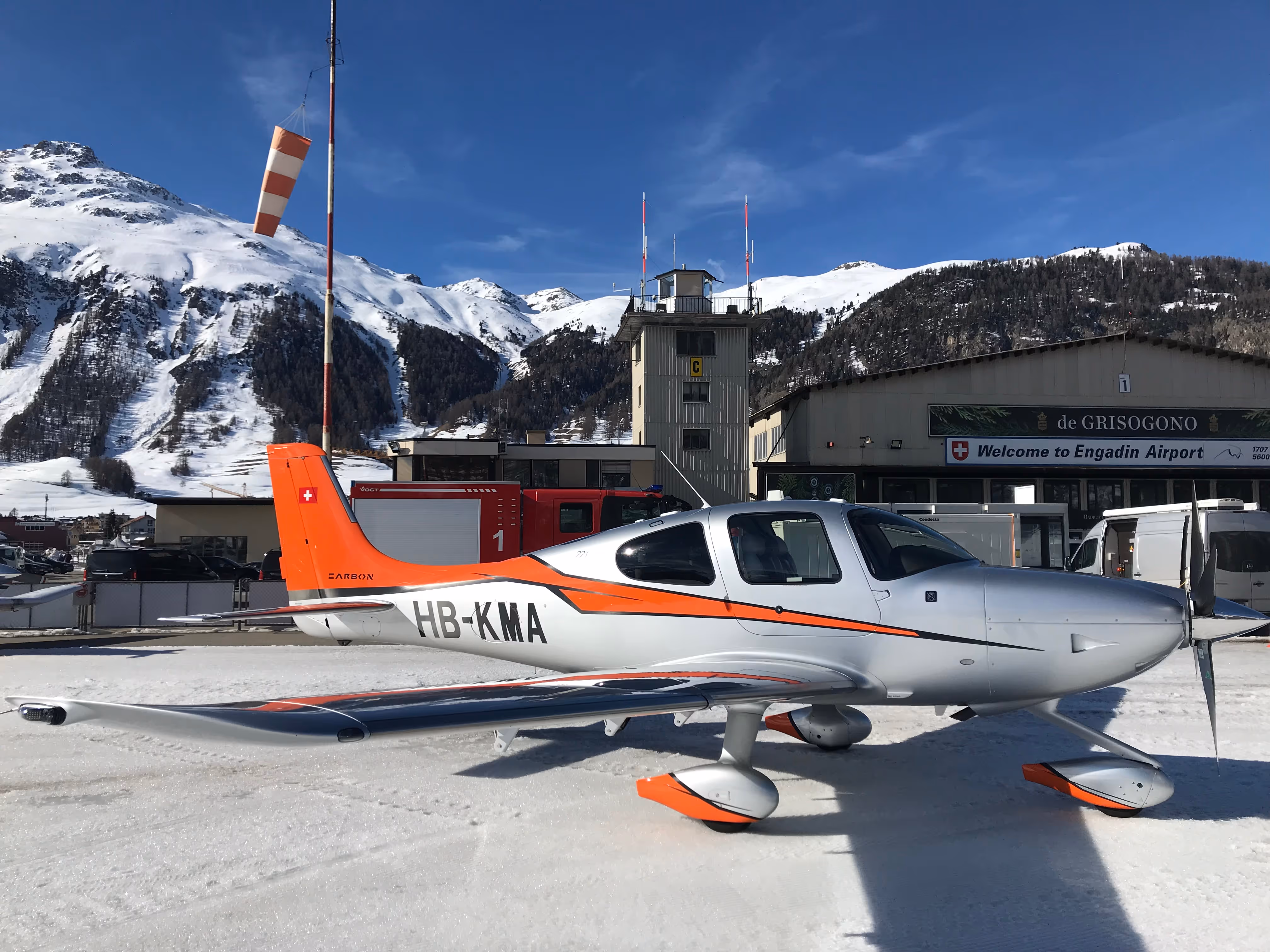 Cirrus SR22 aircraft parked at Engadin Airport with snowy mountains in the background.