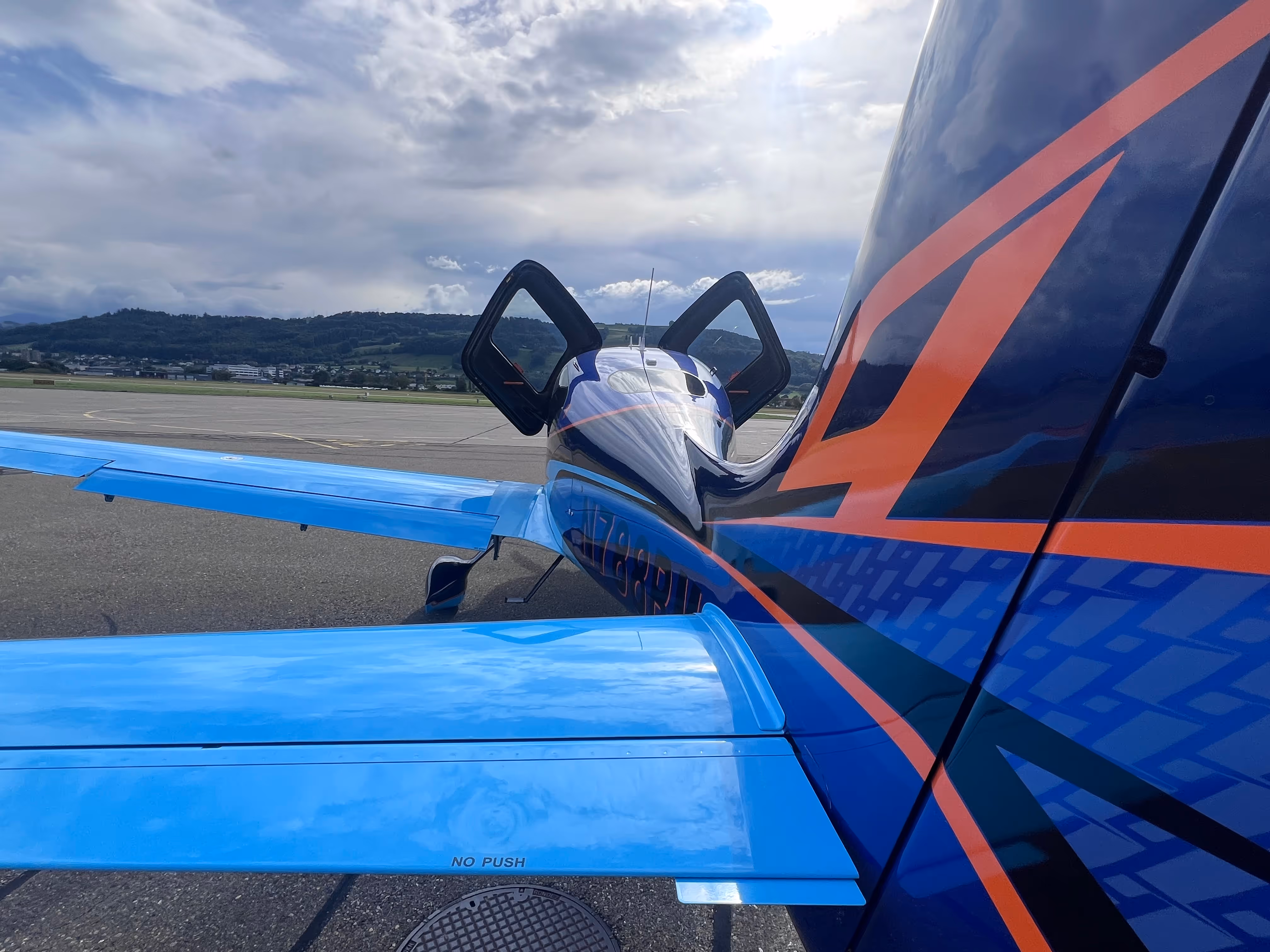 Close-up of Cirrus aircraft with blue and orange custom livery parked on runway.