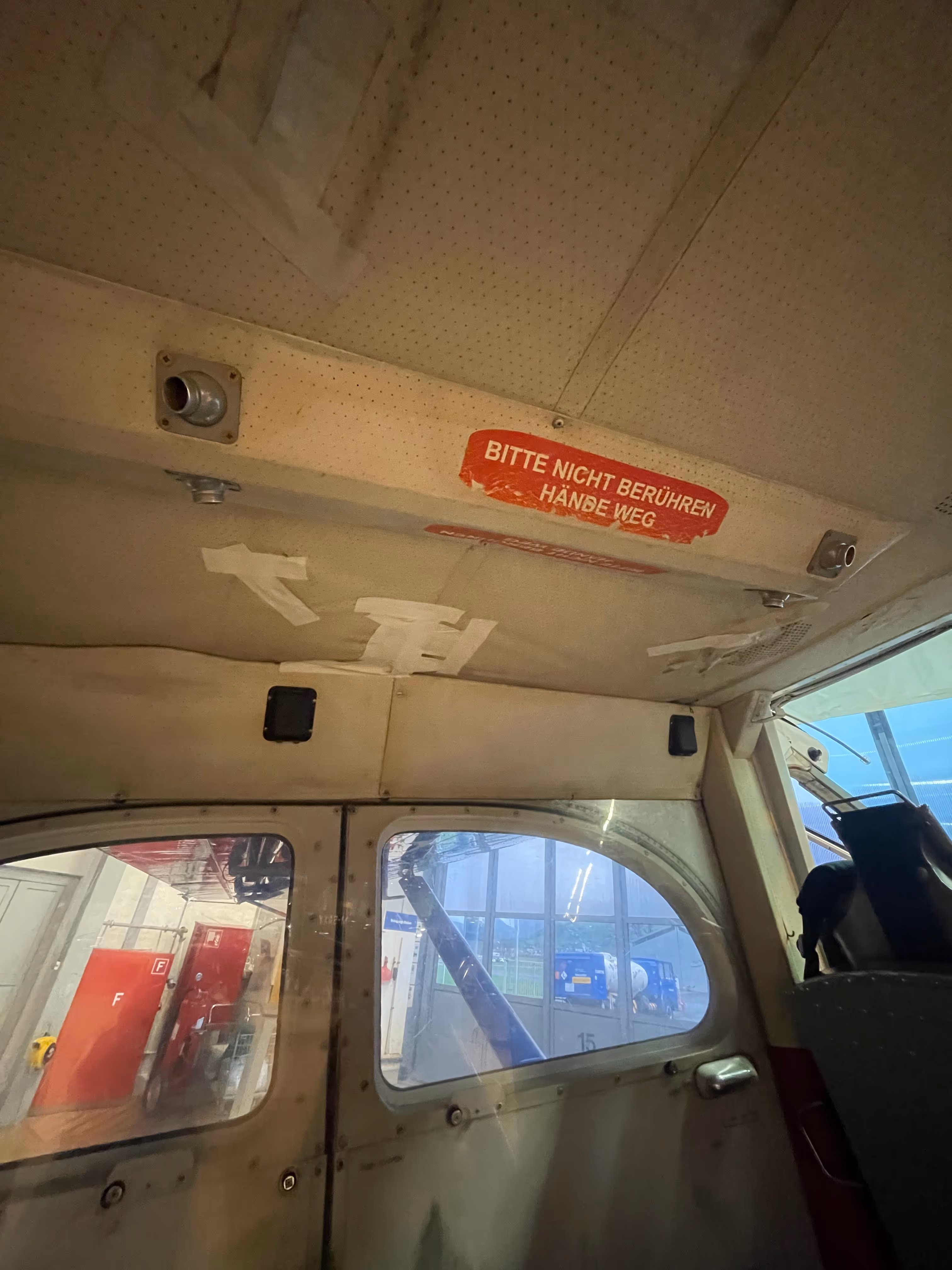 Interior view of small aircraft cabin with German safety sign reading "Bitte nicht berühren Hände weg".