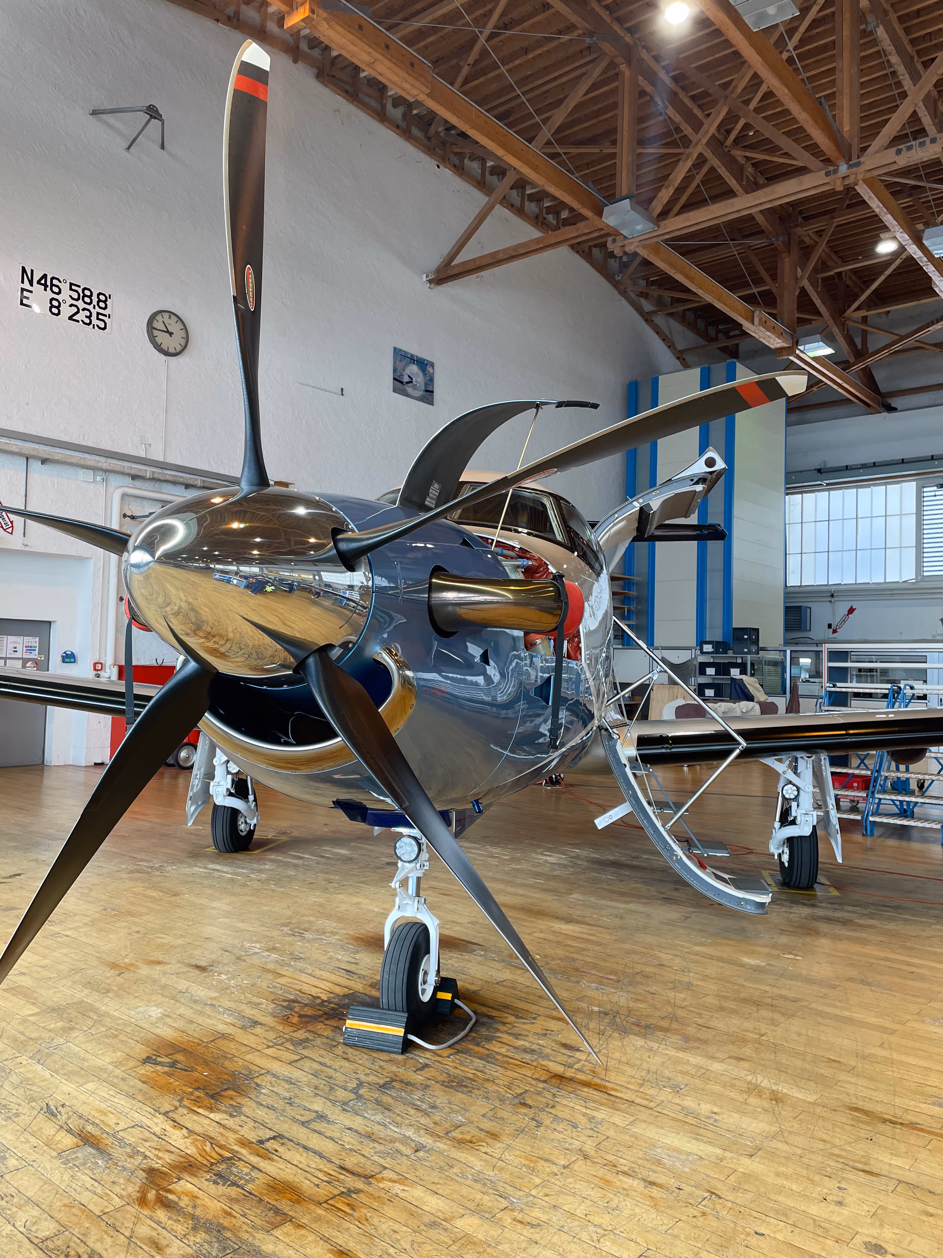 Shiny propeller aircraft parked inside hangar with wooden floor and open doors.
