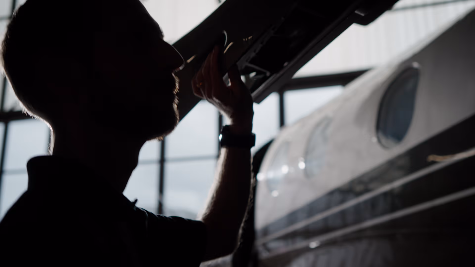 Aircraft mechanic silhouette inspecting plane inside hangar.