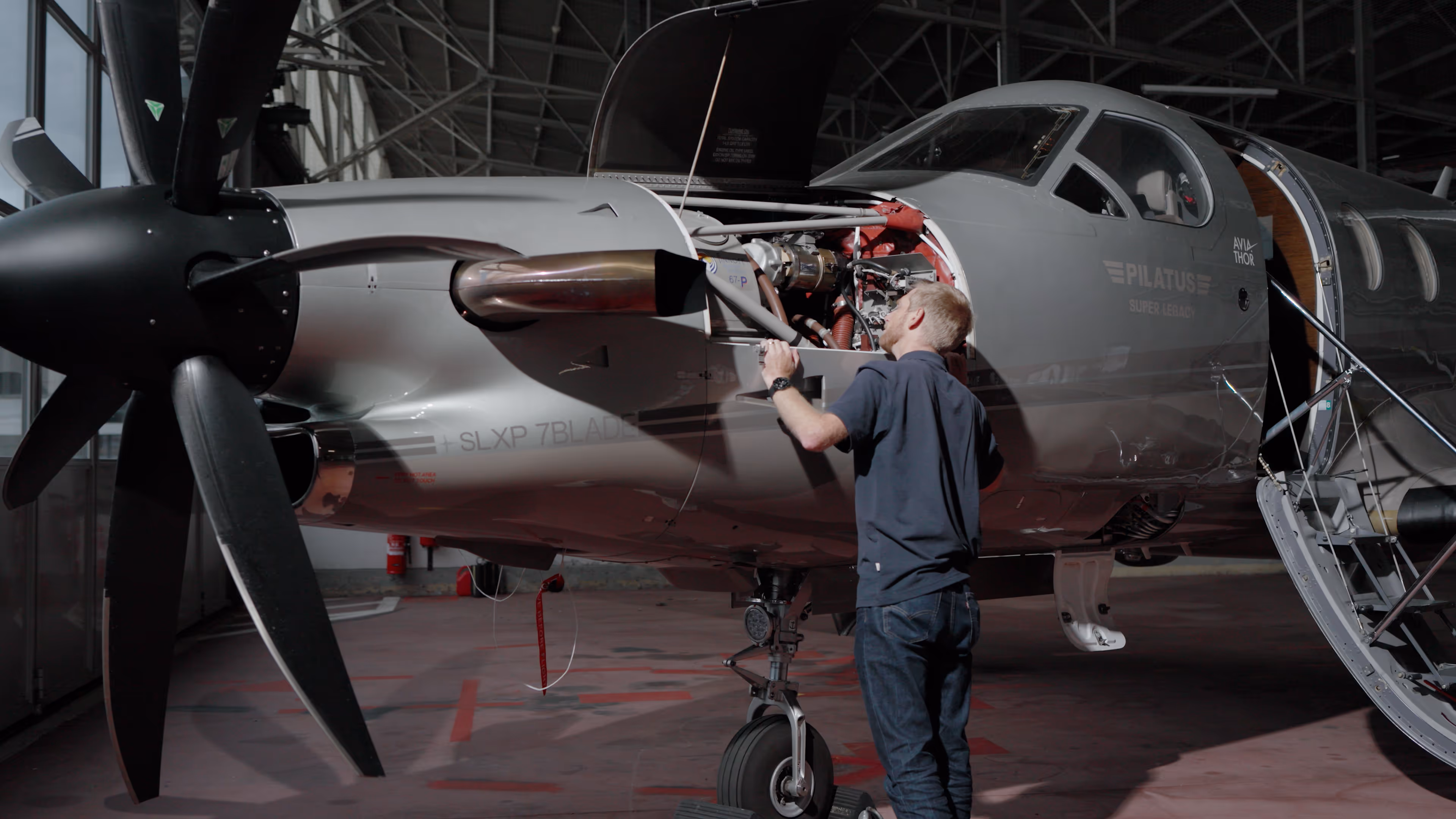 Aircraft mechanic inspecting engine of a Pilatus Super Legacy plane in hangar.