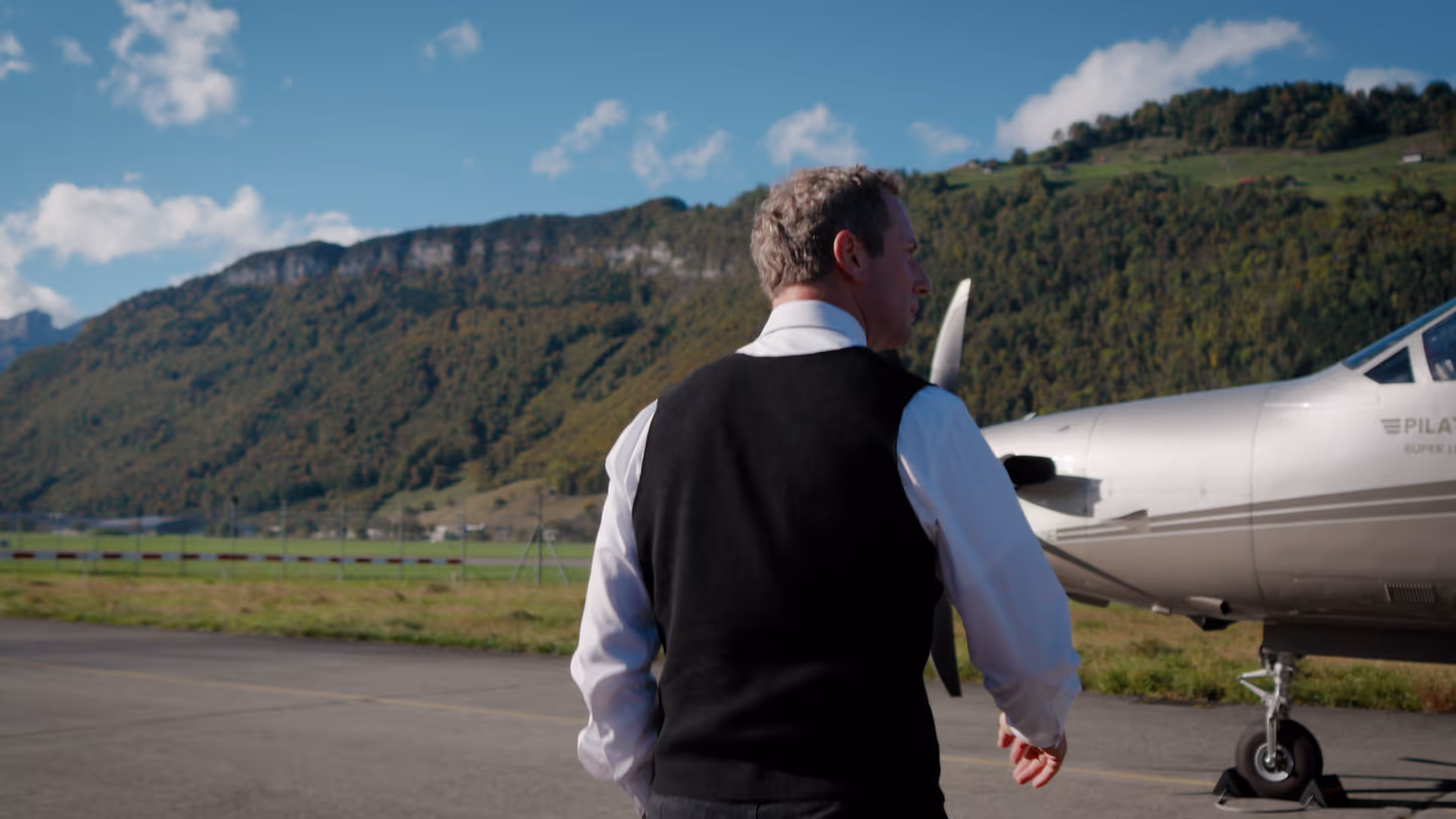 Businessman walking toward a Pilatus aircraft at a mountain airfield.