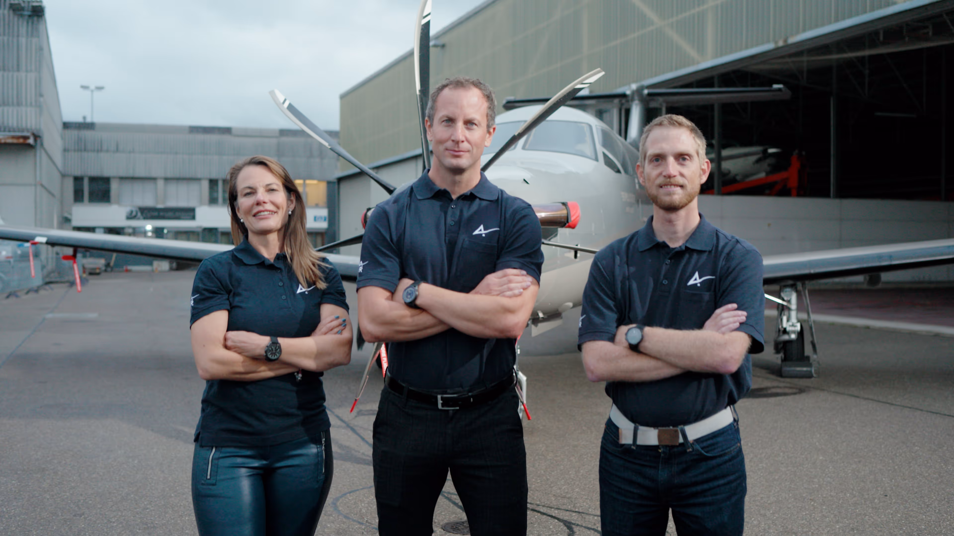 Three aviation professionals posing in front of a Pilatus aircraft with folded arms.