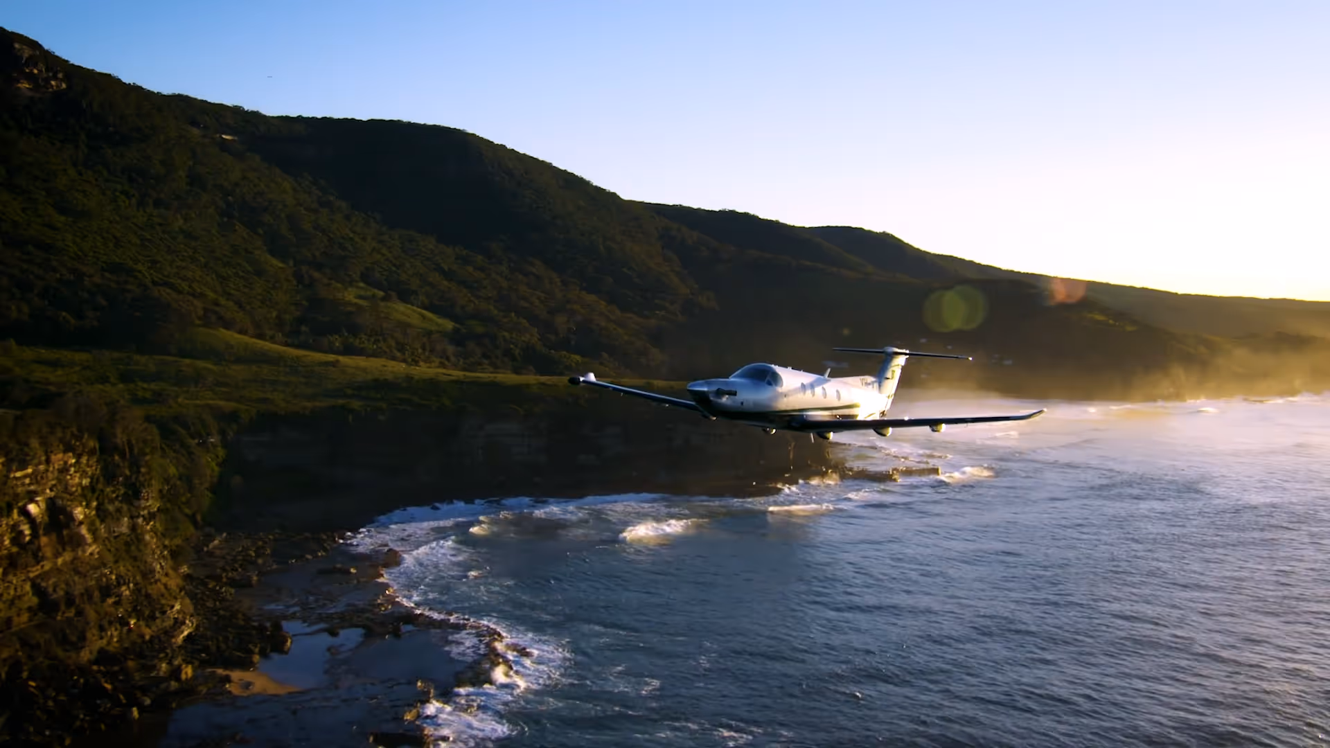 Pilatus PC-12 flying low along coastline at sunset.