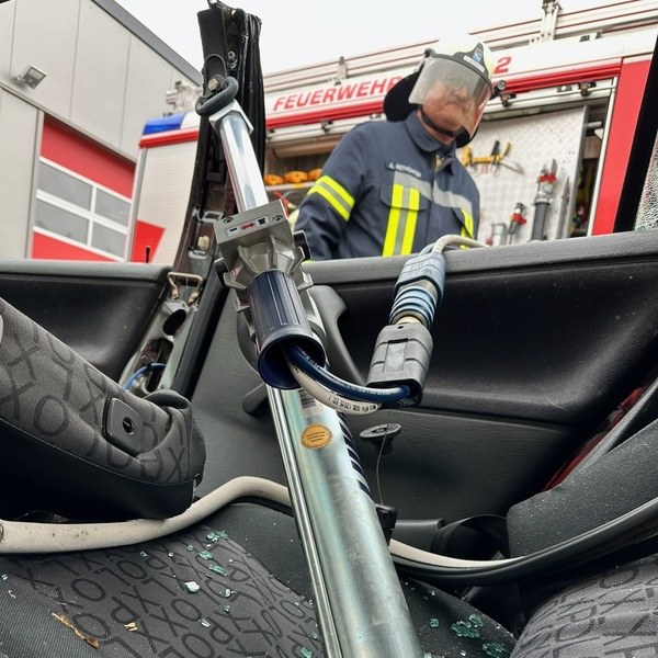 Feuerwehrmann steht neben einem Fahrzeug mit eingeschlagenem Fenster und Rettungsgerät auf dem Vordersitz. PKW Unfallrettung Seminar